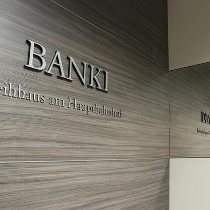 Graue Holzwand mit Firmenname in 3D-Buchstaben Graue Holzwand mit Firmenname in 3D-Buchstaben