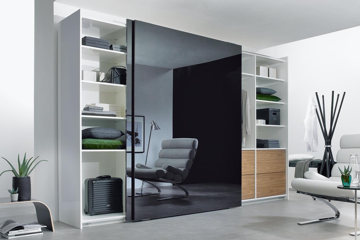Wohnraumimpression mit abgetrennter dunkler Glasschiebetür für Ruheoase und integrierten Einbauregalen